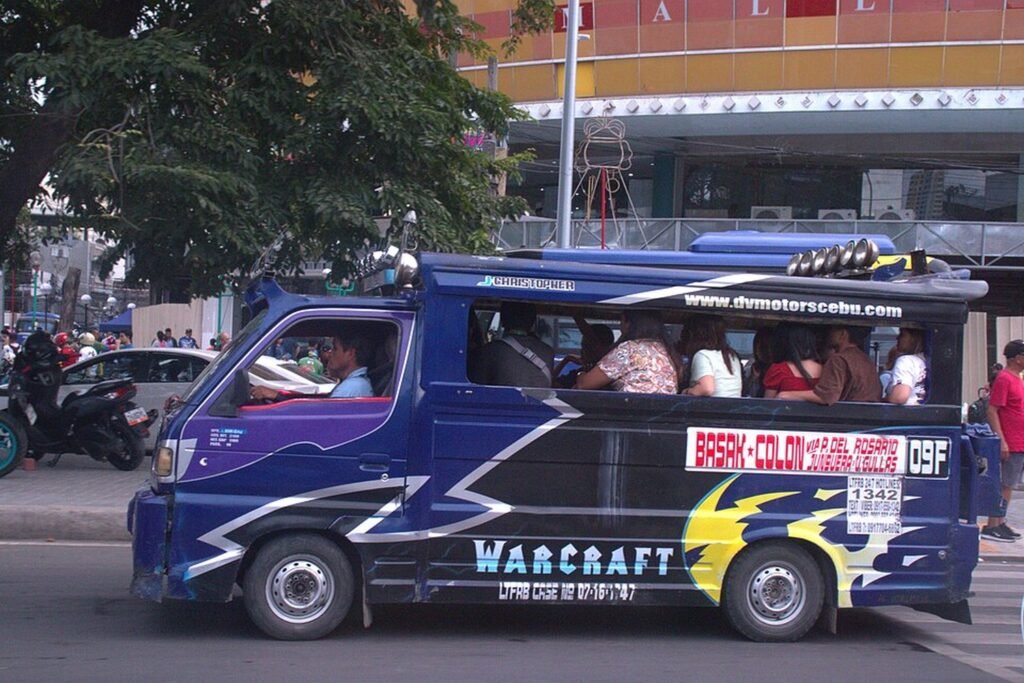 Blue public utility jeepney carrying passengers on a busy street in Cebu City, Philippines.