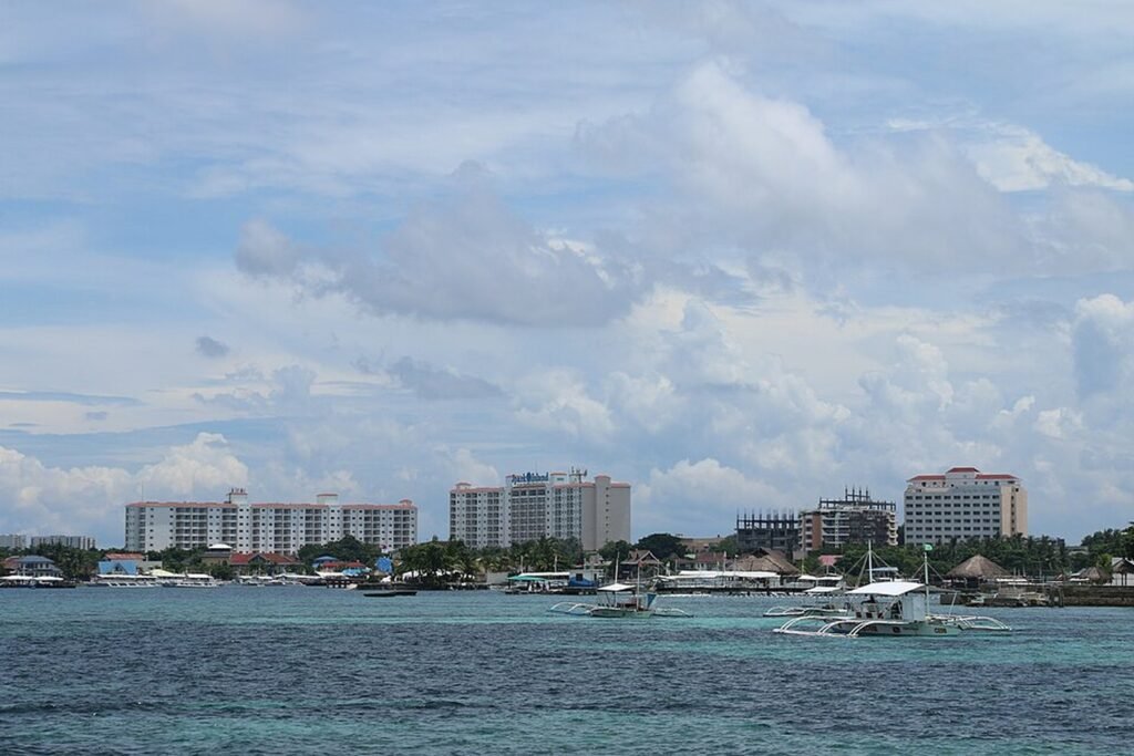 Beachfront hotels and resorts along the Mactan Island coastline in Cebu, with boats on the turquoise water.
