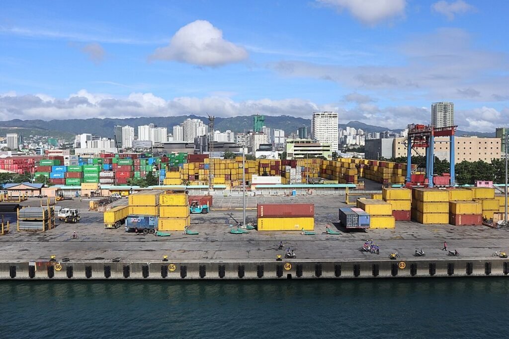 Cebu Port Pier 5 with colourful shipping containers, cargo-handling equipment and Cebu City skyline in the background.